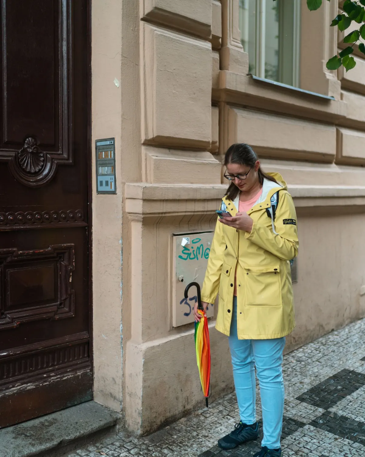 Une femme en imperméable jaune regarde son téléphone dans la rue.